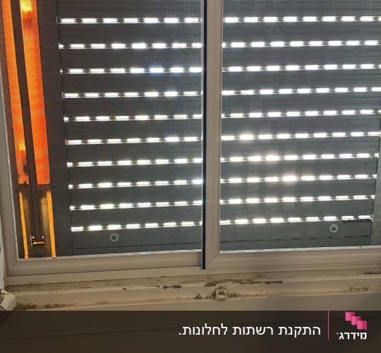 חלון עם תריסים סגורים ומיטה לידו